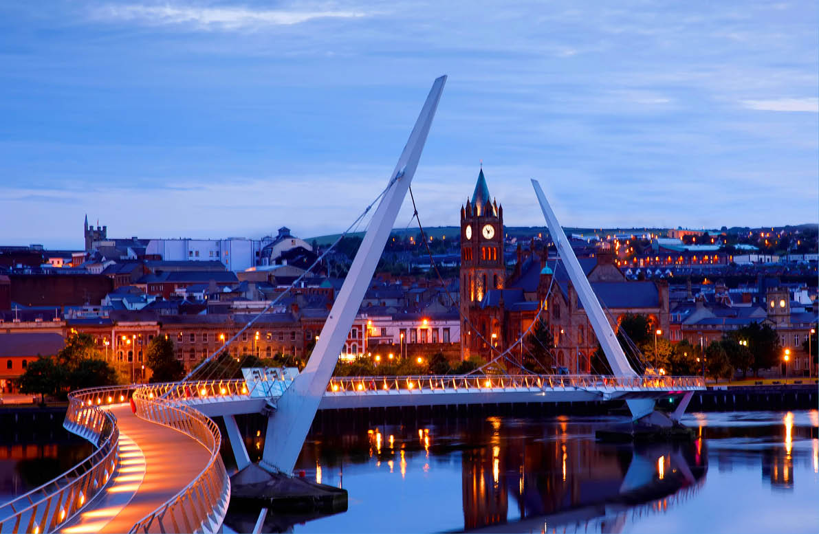 Derry, Ireland  Illuminated Peace bridge in Derry Londonderry, City of Culture, in Northern Ireland with city center at the background  Night cloudy sky with reflection in the river at the dusk