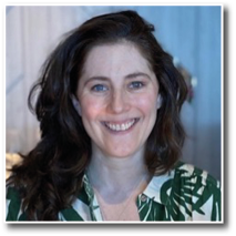 A person with long wavy hair is smiling and wearing a green and white patterned shirt in a softly lit indoor setting. Description generated by AI