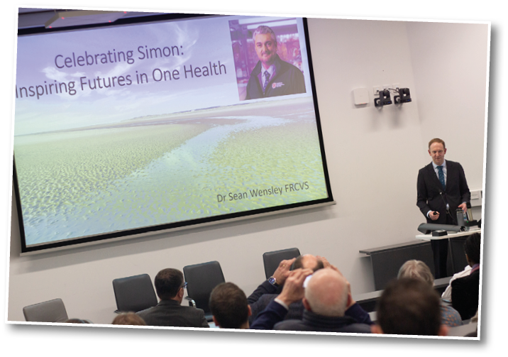 A man in a suit is giving a presentation in front of a screen with a picture of a man on it. AI generated content