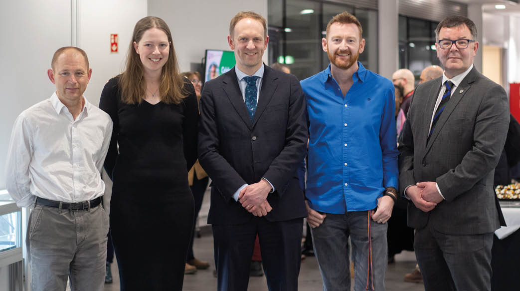 Four people are standing together, posing for a picture. They are all wearing suits and ties, and two of them are wearing blue shirts. The group consists of a man and a woman, both wearing ties, and two other men, one of whom is wearing a blue shirt. AI generated content