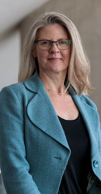 A woman in a blue jacket and black shirt stands in front of a white wall. AI generated content