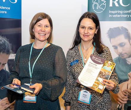 Two adults wearing conference badges stand in front of RCVS banners while holding informational materials at a veterinary care event. Description generated by AI