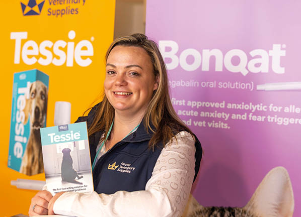 A person wearing a dark vest over a light long-sleeve shirt is holding a product box labeled Tessie in front of promotional banners for Royal Veterinary Supplies and Bonqat. Description generated by AI