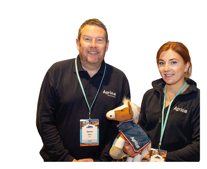 Two people wearing black jackets with name tags are holding a stuffed horse toy dressed in a blue outfit. Description generated by AI