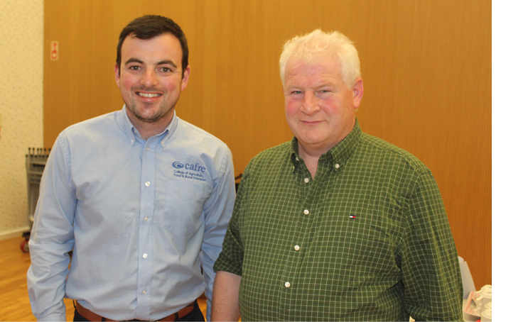 Two adults stand side by side indoors, one wearing a light blue button-up shirt and the other wearing a green checkered button-up shirt, with a wooden wall and patterned wallpaper in the background. Description generated by AI