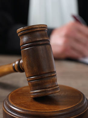 Judge with gavel writing in papers at wooden table, closeup
