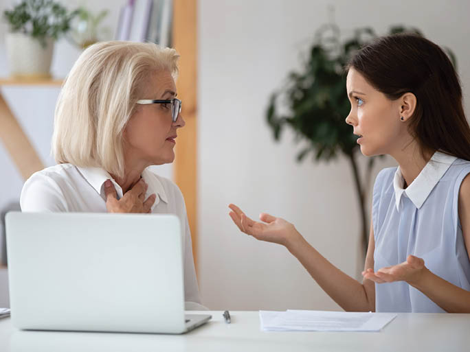 Middle-aged and millennial female colleagues having different opinions on joint project arguing seated at workplace, negative attitude, inequality and discrimination, poor work environment concept
