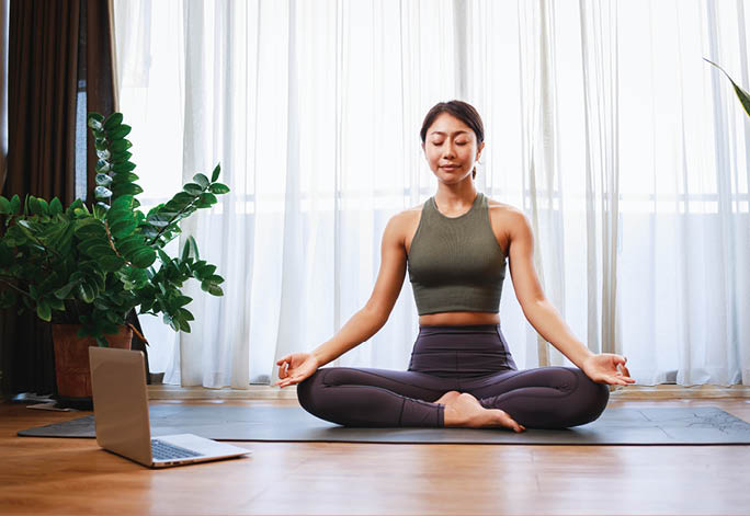 Asian woman practicing yoga from yoga online course on a video conference on a laptop at home. Healthy lifestyle - technology at home. New normal lifestyle