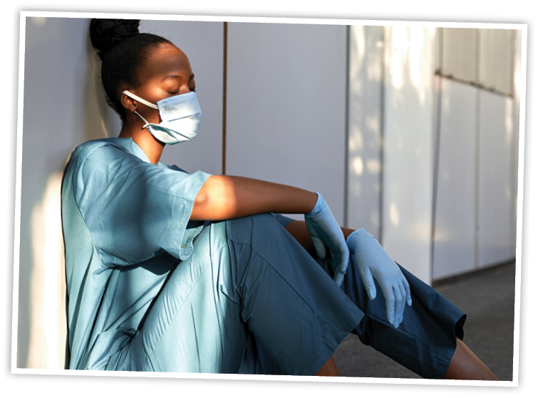 Tired exhausted female african scrub nurse wears face mask blue uniform gloves sits on hospital floor. Depressed sad black ethic doctor feels fatigue burnout stress, lack of sleep, napping at work.